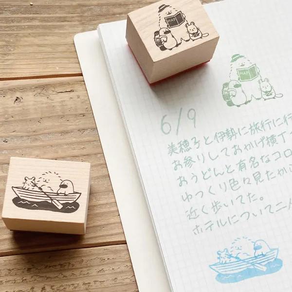 a wooden stamp with a boat illustration and a handwritten note on a notebook with Japanese text.
