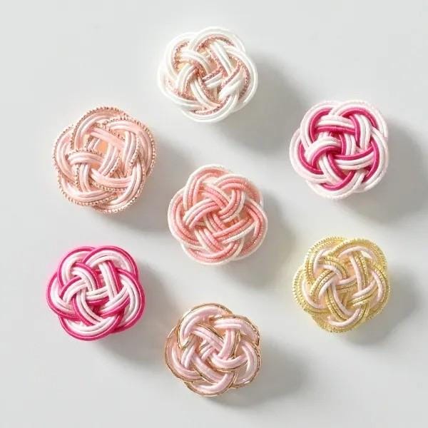 a collection of six intricately knotted flowers in various pastel colors, including pink, white, and gold.