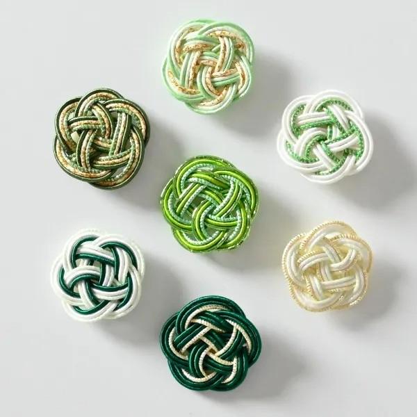 a collection of six intricately knotted flowers in various colors, including green, white, and gold.
