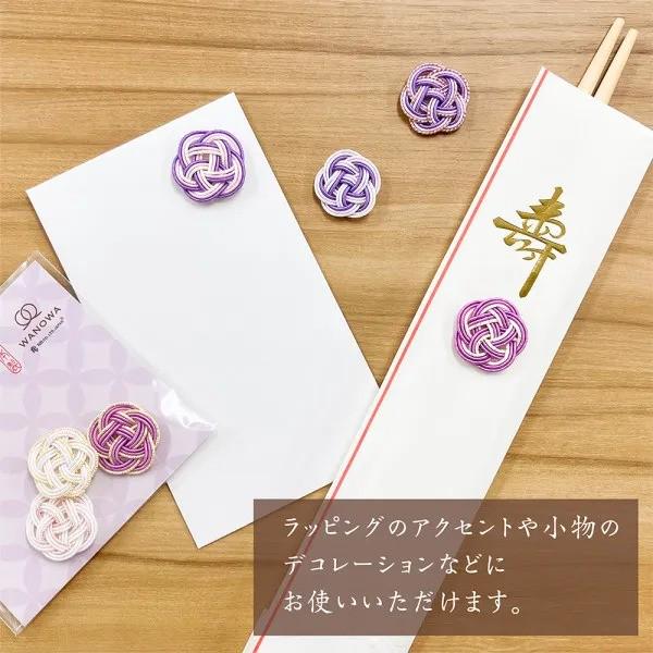 a collection of decorative items, including a white envelope, chopsticks, and several small purple and gold buttons, all placed on a wooden surface.