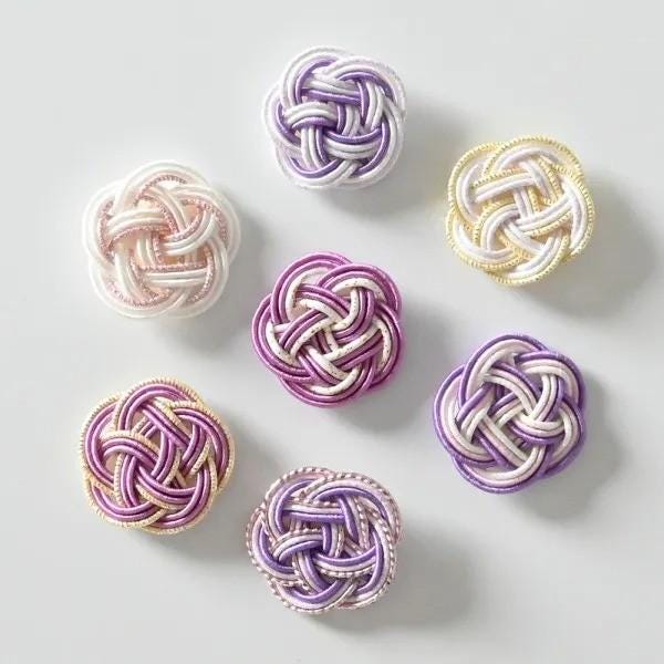 a collection of six intricately knotted buttons in various pastel colors, including white, pink, purple, and yellow.