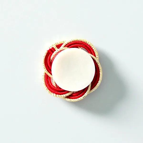 A white candle holder with a red and gold design sits on a white background.