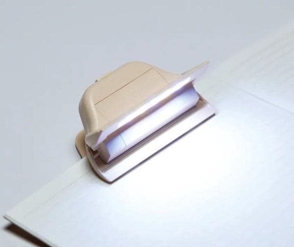 A small, beige paper cutter with a lighted blade is resting on a white surface.