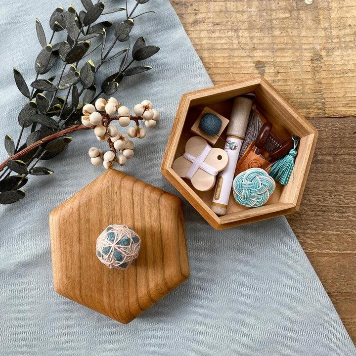 a wooden box with various items, including a ball, a tassel, and some other small objects, placed on a wooden surface.