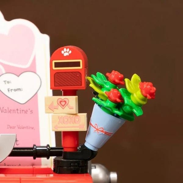 a toy mailbox with a bouquet of flowers attached to it, and there is a Valentine's Day card in the background.