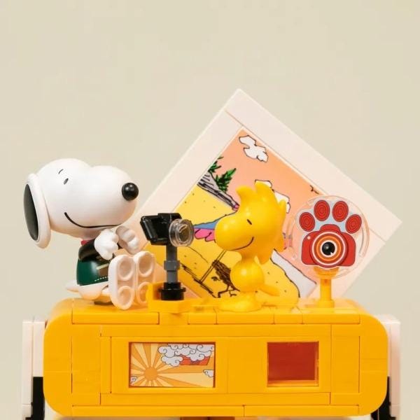 A yellow toy camera with a cartoon character, likely a character from the Peanuts comic strip, sitting on top of it.