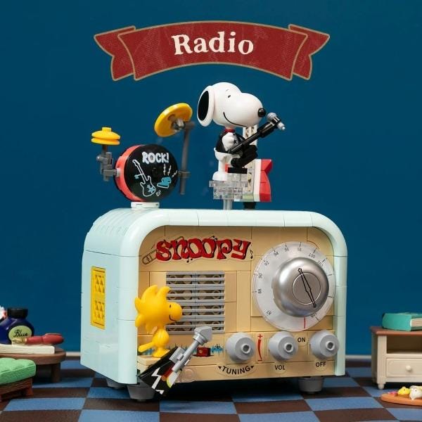 A toy radio with a Snoopy character playing the drums, and a toy guitar, all set against a blue background with a banner that says "Radio".