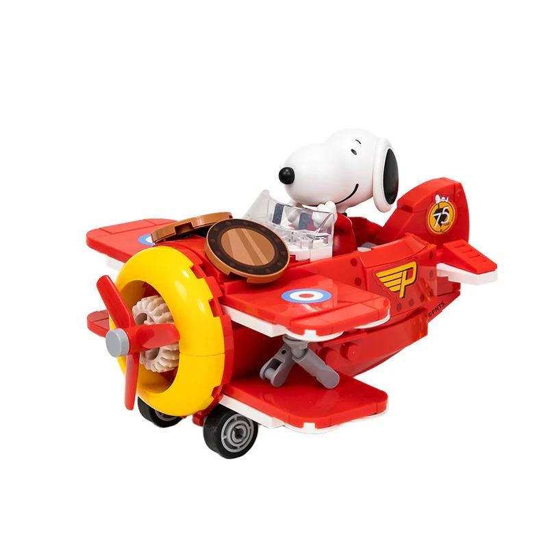 A red and yellow toy airplane with a smiling cartoon character, likely a character from the Peanuts comic strip, sitting in the cockpit.