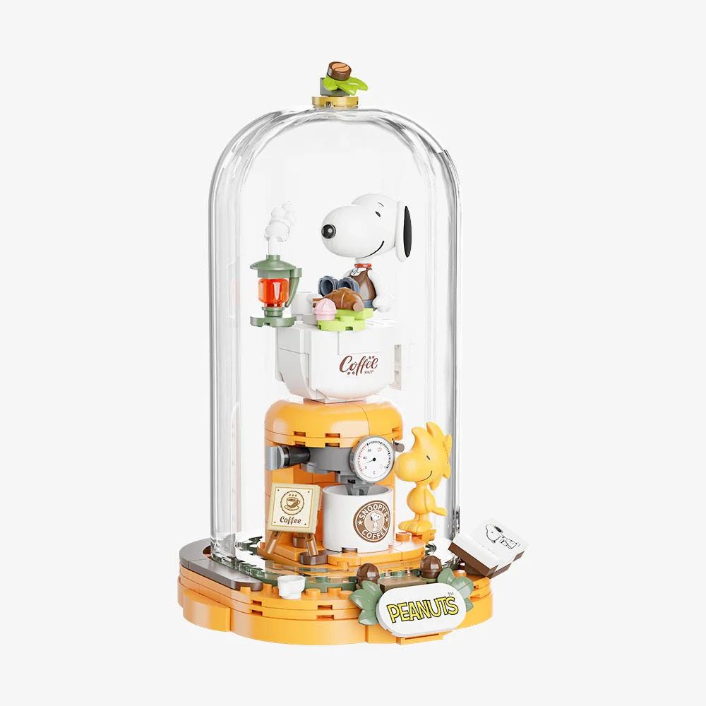 A Peanuts-themed toy with a glass dome containing various Peanuts characters and objects, such as a coffee cup, lantern, and clock.
