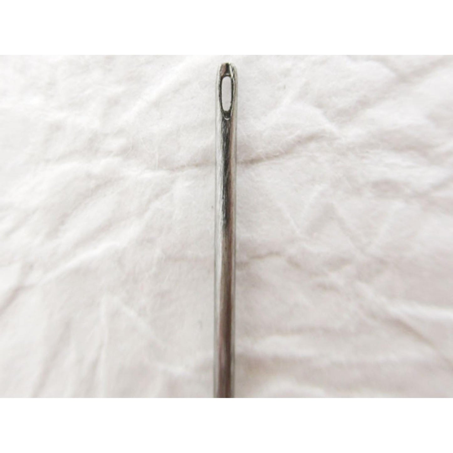 A close-up view of a metal needle with a sharp point, resting on a white surface.