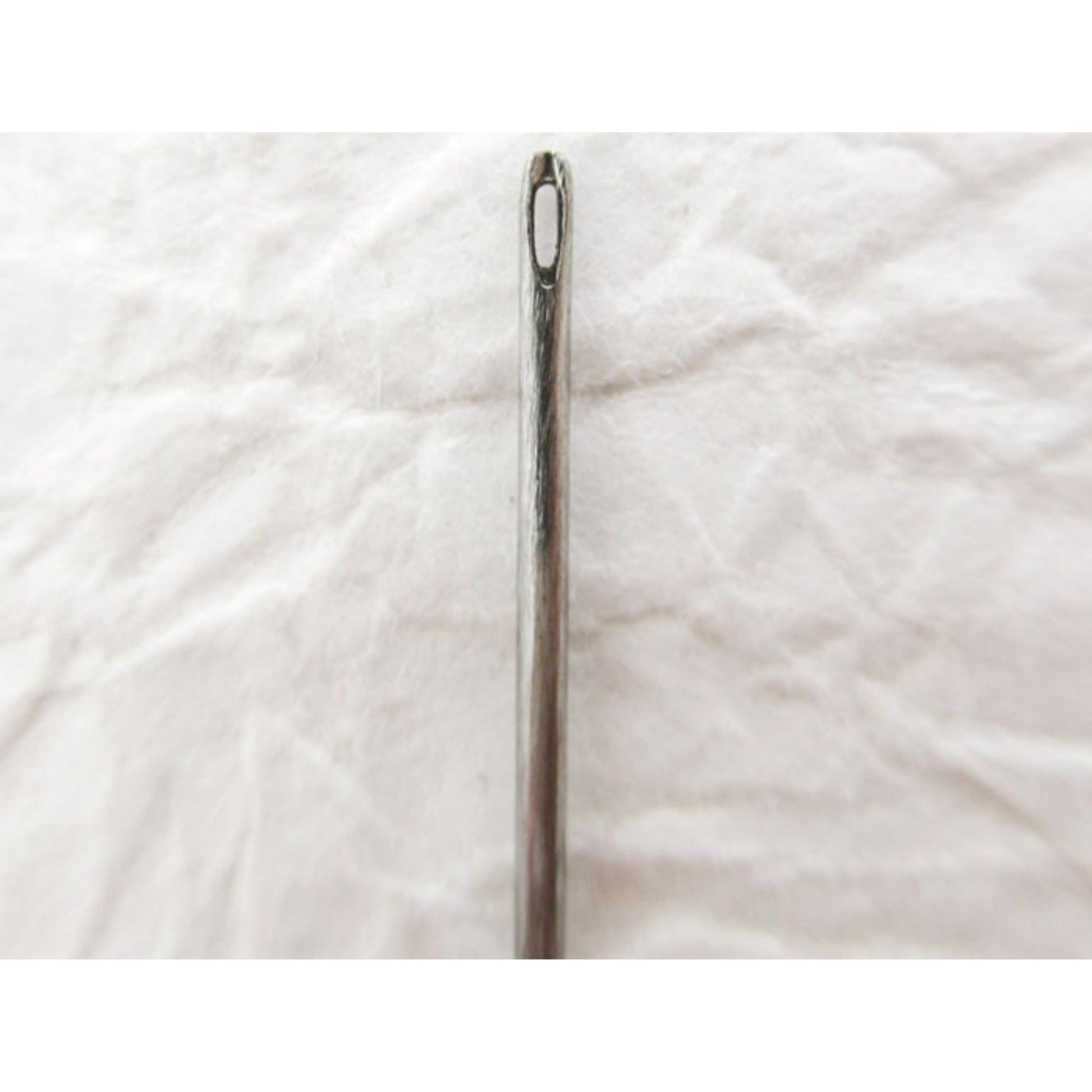 A close-up view of a metal needle with a sharp point, resting on a white surface.