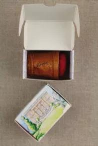 a brown wooden box with a red lid, placed on a gray surface, and a white box with a picture of a building on it.
