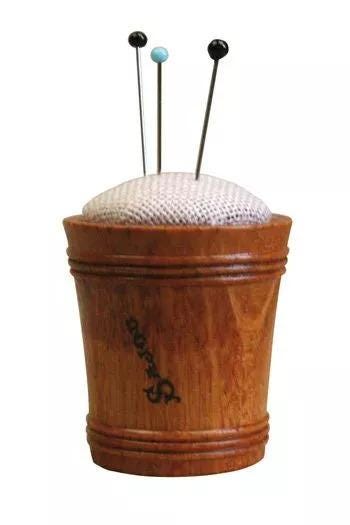 A wooden pin cushion with three needles sticking out of it.