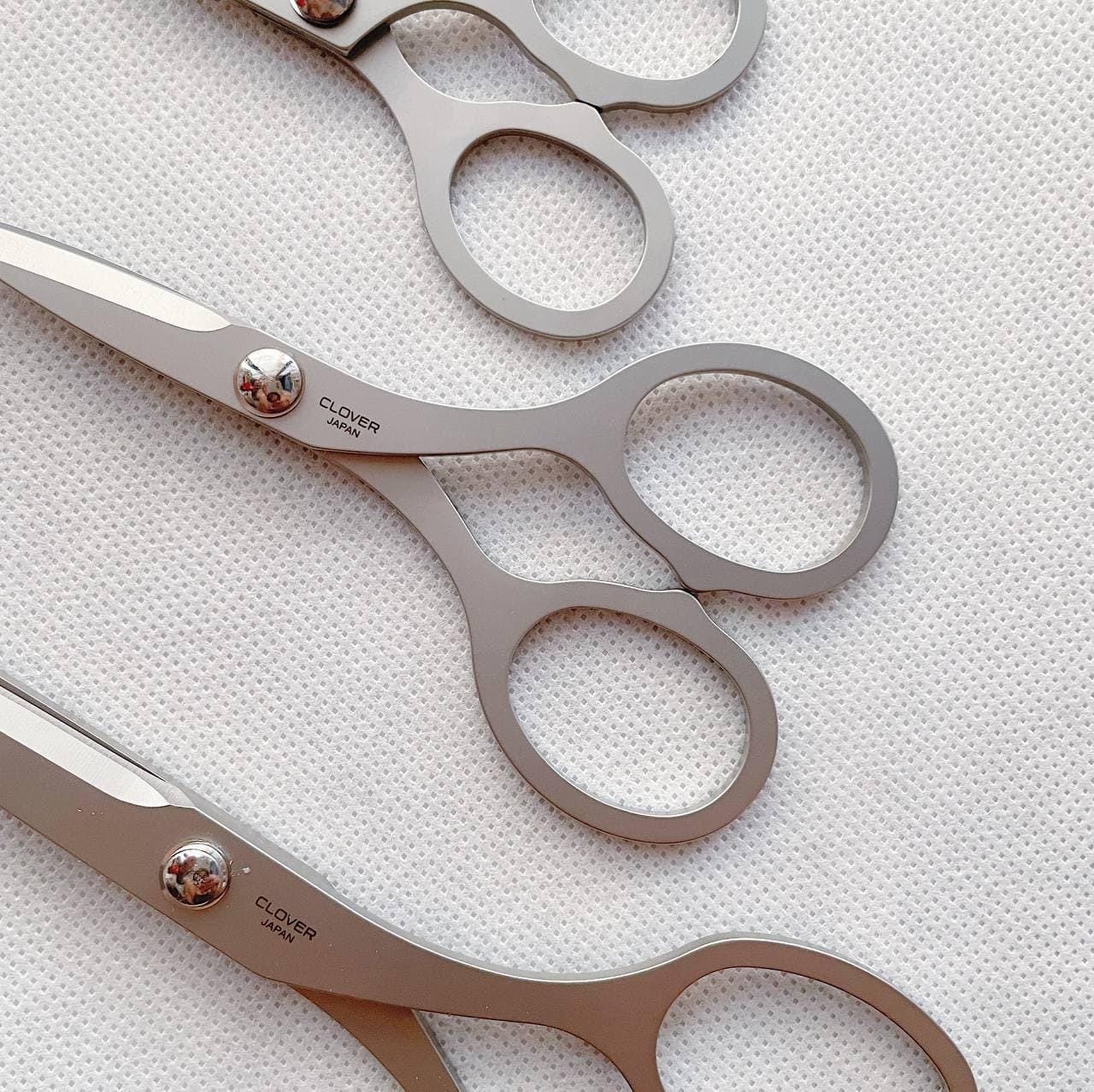 A close-up image of three pairs of silver-colored scissors with the brand name "CLOVER" printed on them.