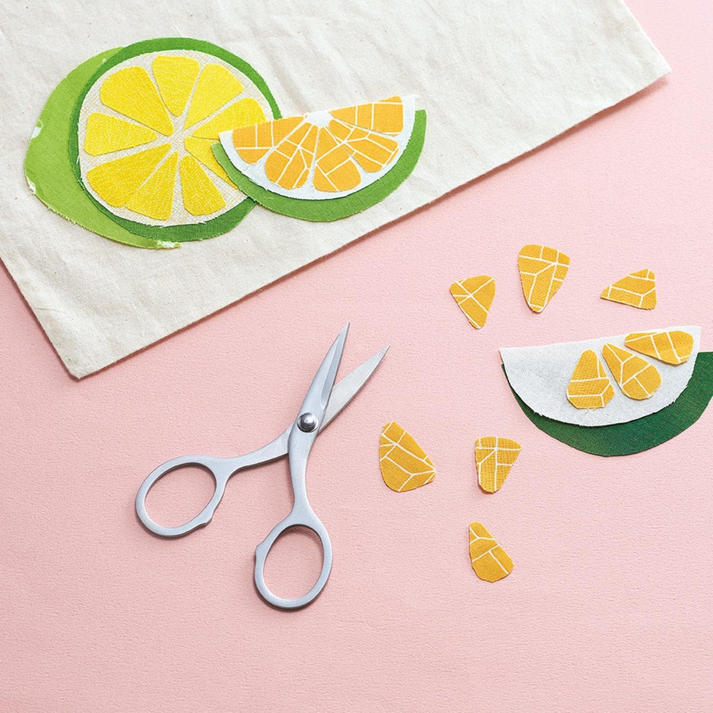 a pair of scissors, a piece of paper with cut-out shapes resembling fruit slices, and some additional cut-out shapes on a pink background.