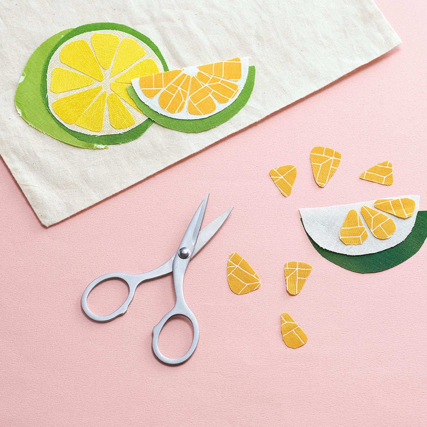 a pair of scissors, a piece of paper with cut-out shapes resembling fruit slices, and some additional cut-out shapes on a pink background.