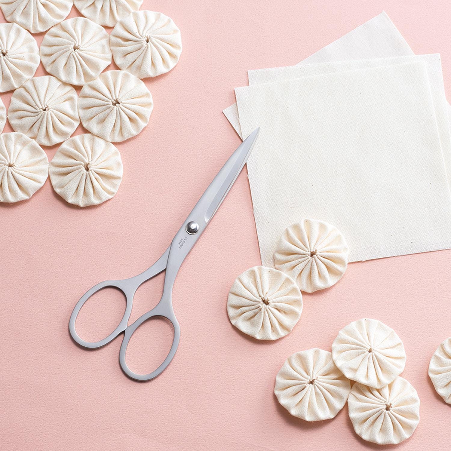 a pair of scissors, white tissue paper, and several white, ruffled shapes arranged on a pink background.