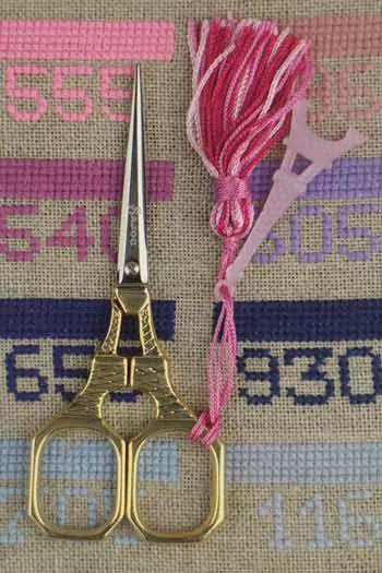 a pair of gold scissors with a pink tassel, placed on a beige background with various numbers and letters.