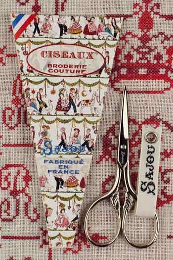 a pair of scissors and a decorative paper with a pattern of people and various objects, all placed on a red and white fabric background.
