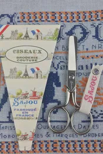 a pair of scissors and a folded piece of paper with a picture of Paris, along with a tag that says "Saujou".