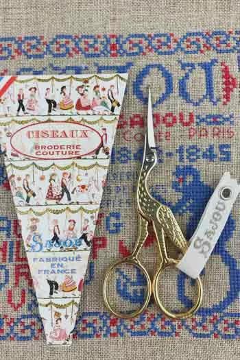 a pair of gold scissors and a decorative paper with a pattern of people and text, all placed on a beige background with a blue and red pattern.