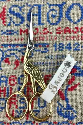 A pair of gold-colored scissors with a white label attached to them, placed on a fabric with a blue and red pattern.