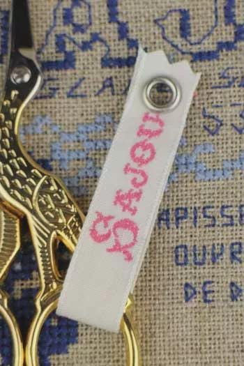 a pair of gold scissors with a white tag attached to them, resting on a piece of embroidered fabric.
