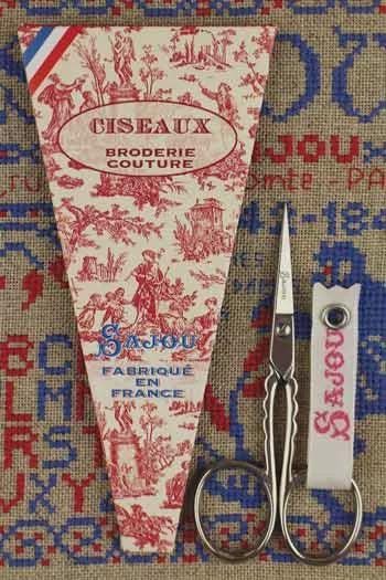 a pair of scissors, a package of fabric, and a needle and thread, all arranged on a patterned fabric background.