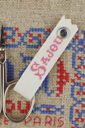 a pair of scissors with a white tag attached to them, which has the word "PARIS" written on it.