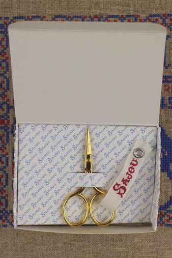 a pair of gold scissors placed inside a white box with a blue and red patterned design.