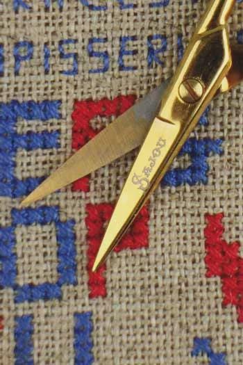 A pair of gold scissors rests on a beige fabric with blue and red embroidered patterns.