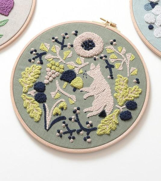 a circular embroidery piece with a floral design, including a pink flower, green leaves, and other decorative elements.
