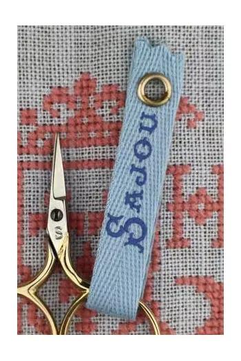 A pair of gold scissors with a blue handle and a matching blue tag with the word "Sandy" printed on it, placed on a red and white fabric background.