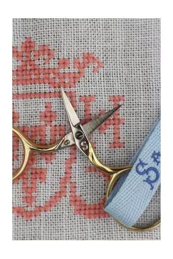 A pair of gold-colored scissors with a blue strap is resting on a gray and red embroidered fabric.