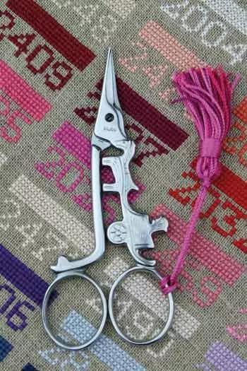 A pair of silver scissors with a pink tassel is placed on a colorful fabric with various patterns.