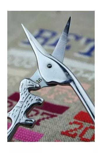A pair of silver scissors with a pointed tip and a curved blade, resting on a surface with a patterned background.