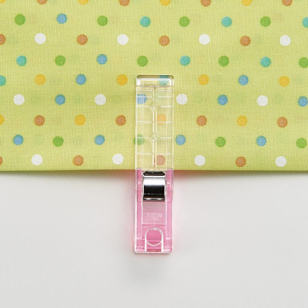 A clear plastic sewing clip is attached to a fabric with a colorful polka dot pattern.