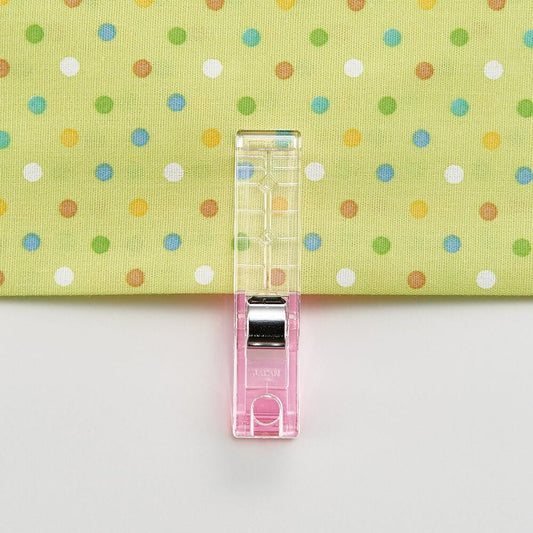 A clear plastic sewing clip is attached to a fabric with a colorful polka dot pattern.