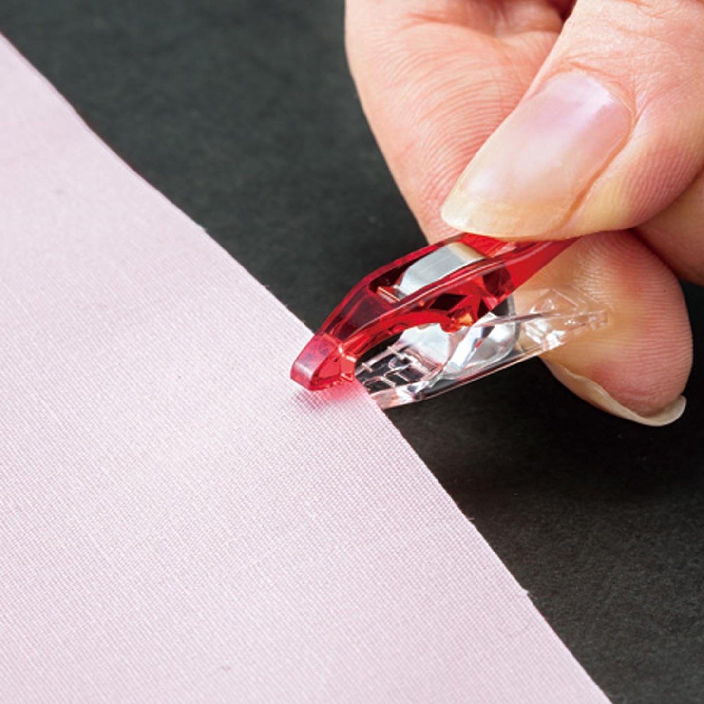 A hand is using a red and silver tool to cut a pink fabric, which appears to be a piece of paper or fabric.