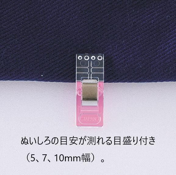 A pink plastic clip with a clear plastic attachment, placed on a dark fabric surface.