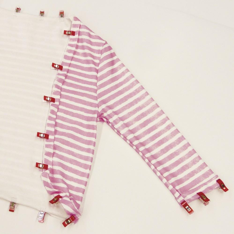 a pink and white striped shirt with red clips fastening the sleeves, laid out on a white surface.