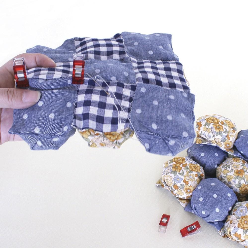 A hand is holding a quilt with red and white clasps, surrounded by additional quilts with blue and white polka dot patterns.