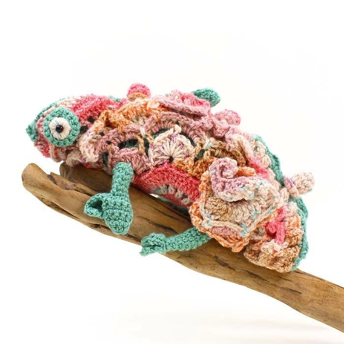A crocheted chameleon toy is sitting on a wooden stick.