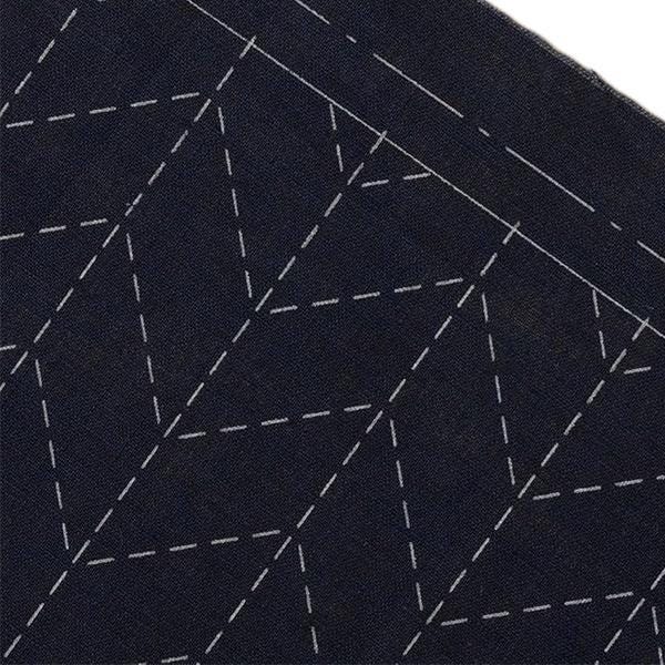 a close-up view of a dark fabric with a geometric pattern of white lines and dots, creating a visually striking contrast against the dark background.