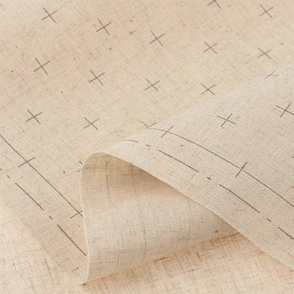 a close-up view of a fabric with a repeating pattern of black crosses on a beige background.