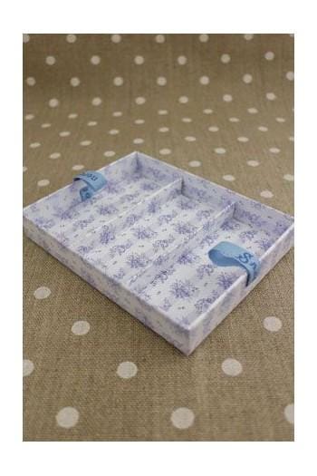 A white and blue patterned box with blue handles, placed on a beige fabric with white polka dots.