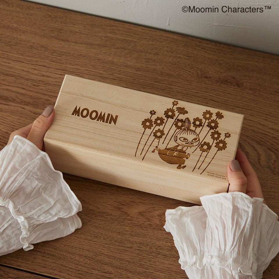 A person's hands holding a wooden box with a floral design and the word "Moomin" printed on it.
