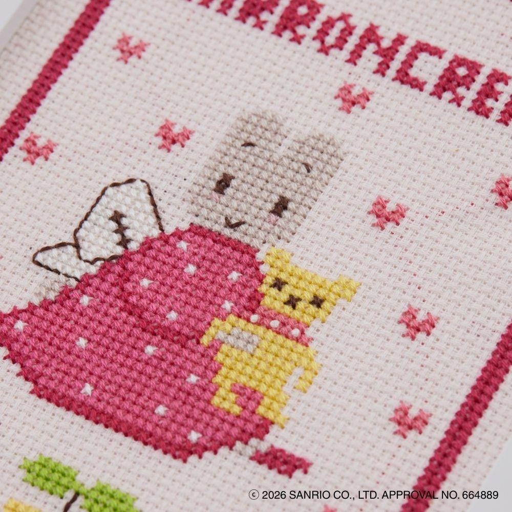 The image is a close-up of a cross-stitch pattern featuring a pink dress with a small yellow cat and a gray rabbit. The pattern is set against a pink background with small red flowers scattered throughout.