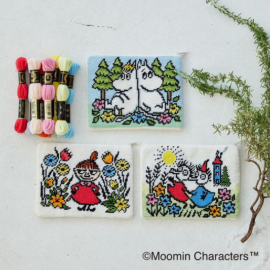 three cross-stitch designs featuring characters from the Moomin character series, including Minnie Mouse, Moomin, and other beloved characters. The designs are arranged on a white background, with a plant and a spool of thread visible in the background.