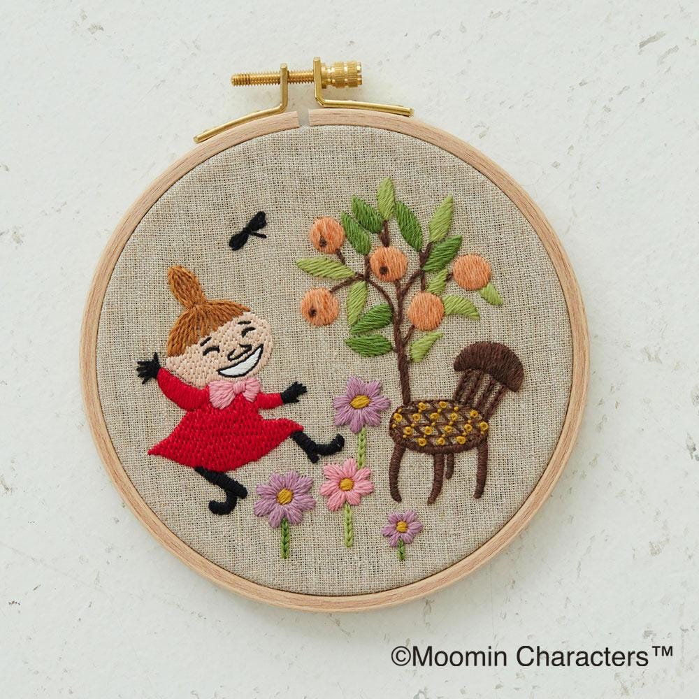a hand-embroidered scene of a young girl in a red dress, surrounded by flowers, a tree, and a chair.